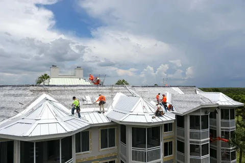 Professional roofing crew installing a metal roofing system on a multi-unit residential building under clear sky conditions.