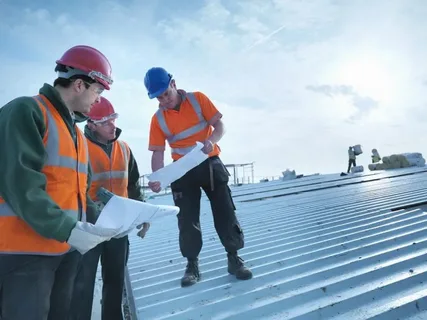 Construction workers reviewing plans on a metal roof.